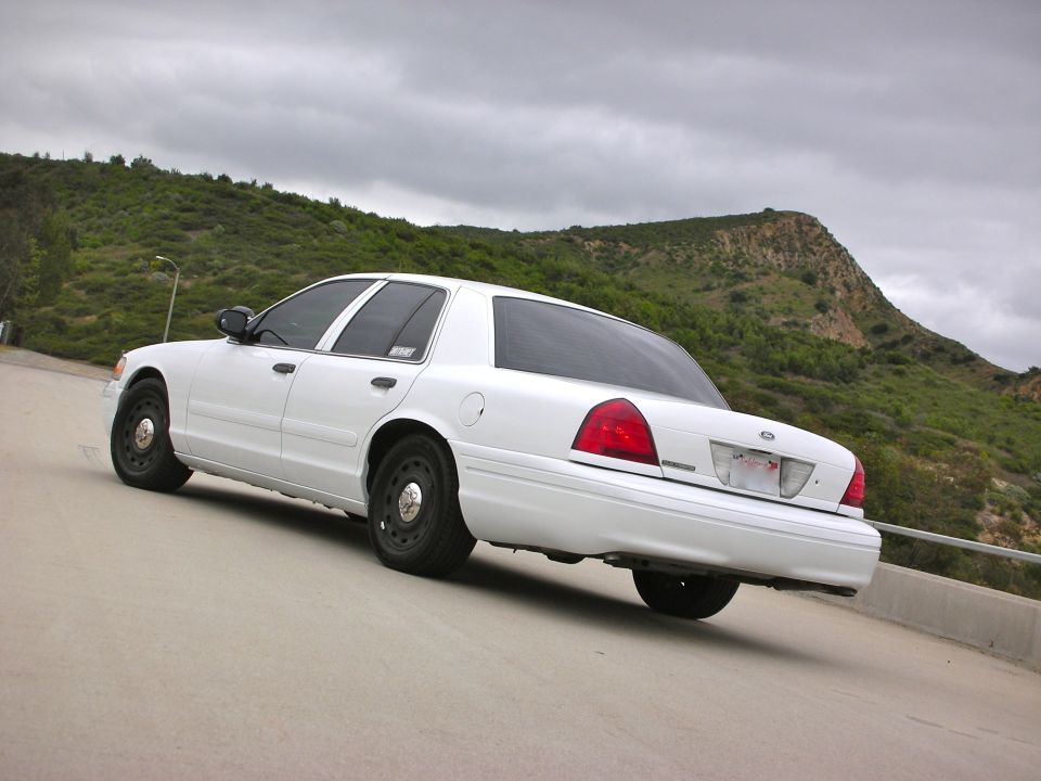 White 2004 Ford Crown Victoria parked on a road with a hill in the background
