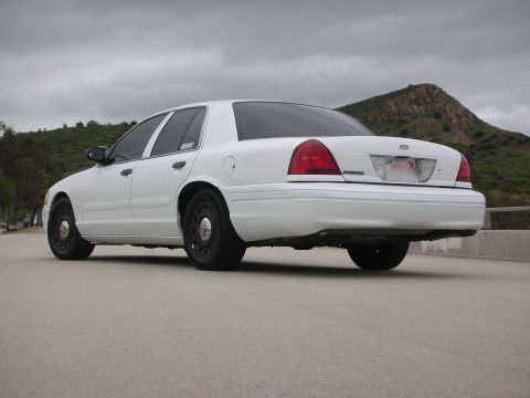 2004 Ford Crown Victoria - A white sedan is viewed from the rear, parked on a paved surface with a hilly landscape in the background.