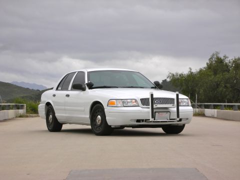 2004 Ford Crown Victoria - A white 2004 Ford Crown Victoria police car is parked on a road, facing forward with a push bar on the front.