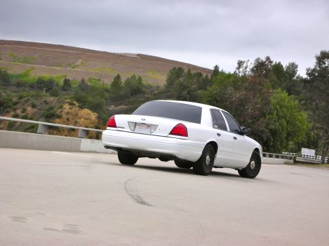 2004 Ford Crown Victoria - A white sedan is seen from the rear on a paved surface with a tire mark.