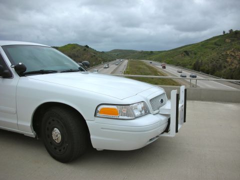 2004 Ford Crown Victoria - A white 2004 Ford Crown Victoria police car is parked on an overpass overlooking a busy highway.