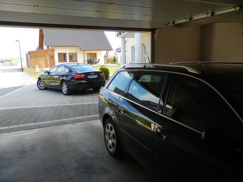 2010 Audi A4 - Two dark-colored Audi vehicles are parked in a driveway, one in the foreground and another further back.