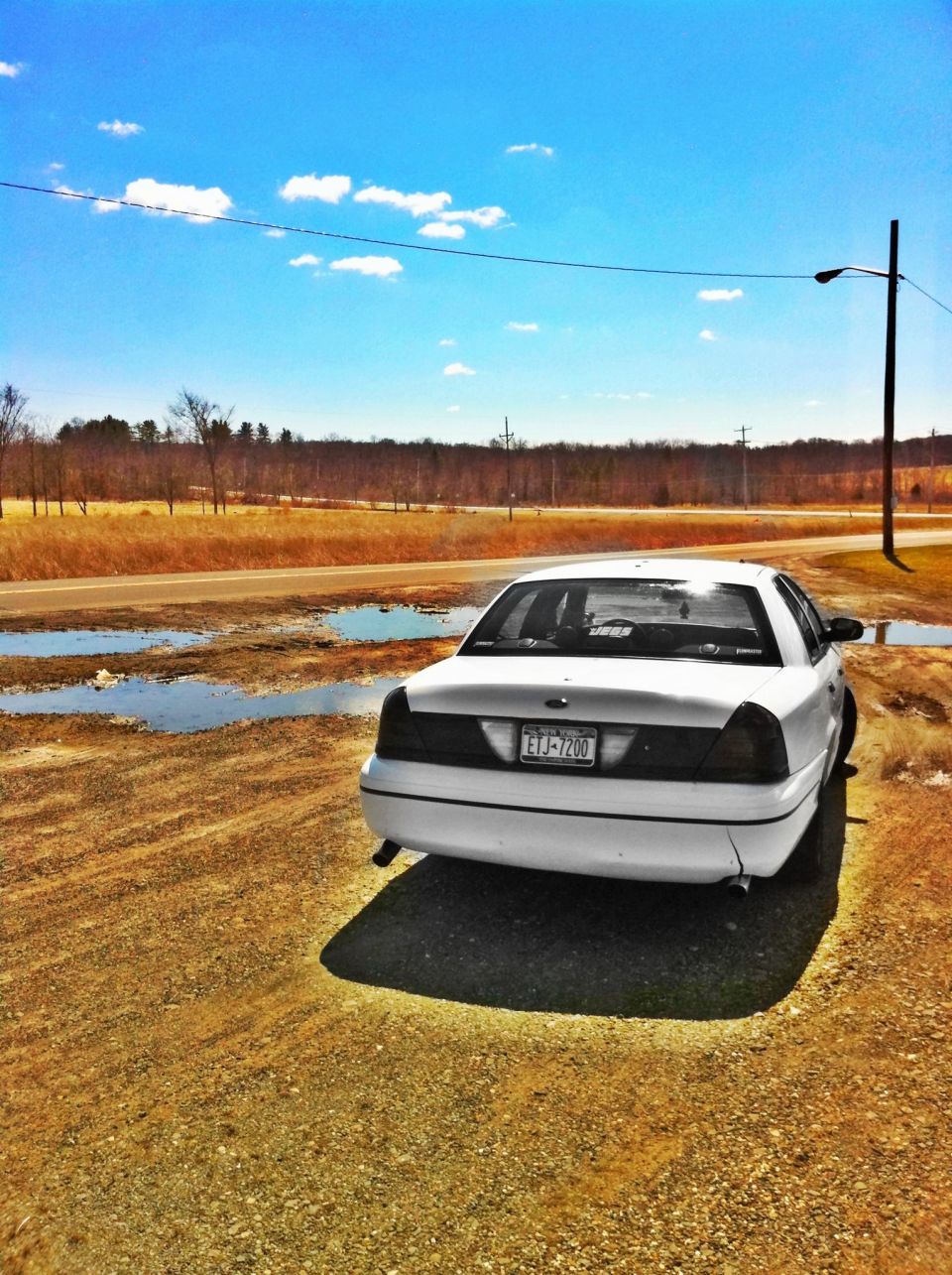 White 2000 Ford Crown Victoria parked on gravel with puddles, rear view