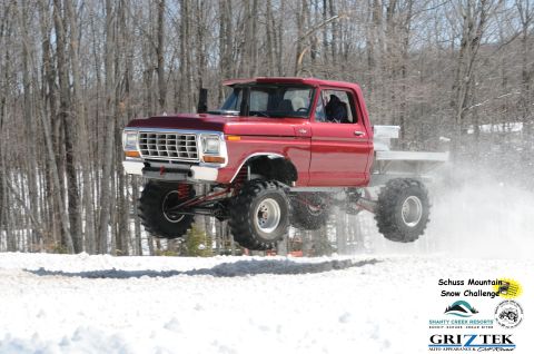 1978 Ford F-150 - A modified red pickup truck jumps over a snowy terrain during a winter event.