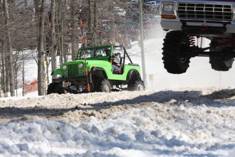 1978 Ford F-150 - Two modified trucks jump over a snowy terrain during an off-road event.