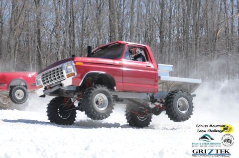 1978 Ford F-150 - A red pickup truck with large tires is airborne during a snow event, kicking up snow.