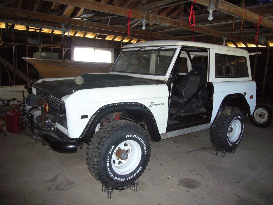 1973 Ford Bronco in garage with doors open, hood is black, BFGoodrich tires