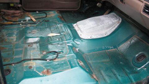 1992 Ford Bronco - The interior floor of a vehicle is shown with seats removed, revealing rust and exposed wiring.