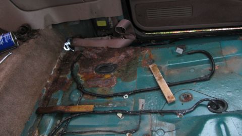 1992 Ford Bronco - The interior floor of a vehicle shows significant rust and damage, with wiring exposed.
