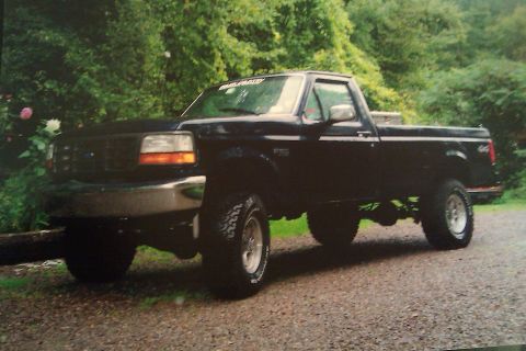 1993 Ford F-150 - This black Ford F-150 pickup truck is shown from a three-quarter front angle, with a lifted suspension and off-road tires.