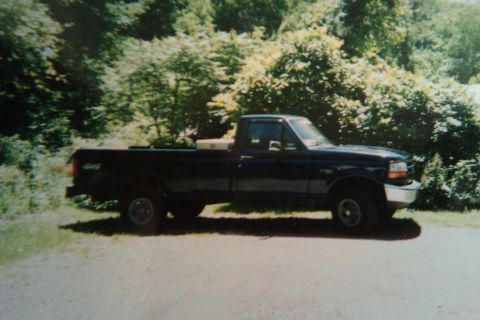 1993 Ford F-150 - Side view of a dark blue 1993 Ford F-150 pickup truck parked outdoors with trees in the background.