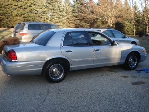 2000 Ford Crown Victoria - A silver 2000 Ford Crown Victoria sedan is parked outdoors next to another vehicle.