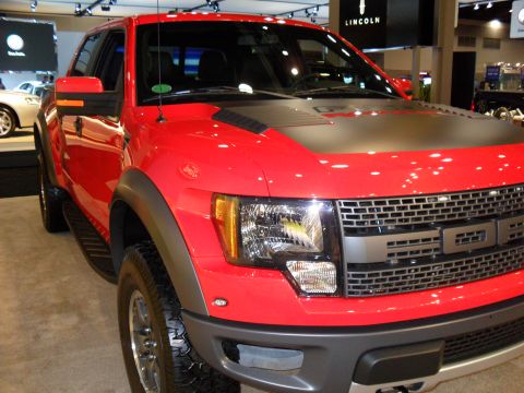 2011 Ford F-150 - A red Ford F-150 Raptor truck is displayed indoors, with 'LINCOLN' visible in the background.