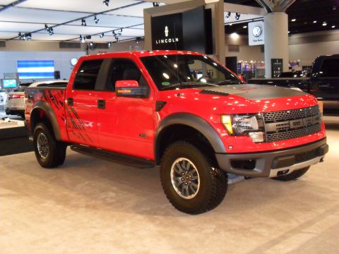 2011 Ford F-150 - A red 2011 Ford F-150 Raptor pickup truck is displayed at an auto show.