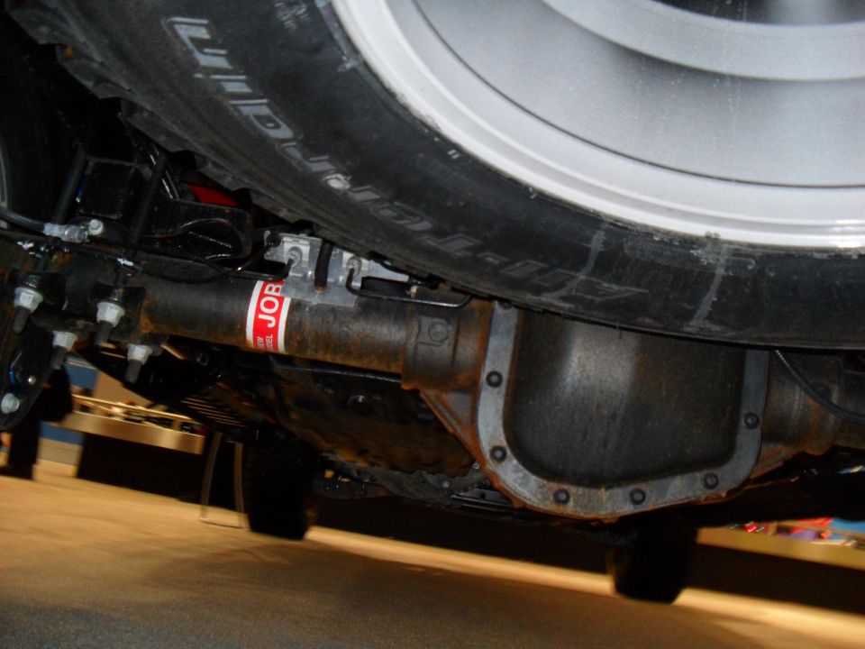 Underside view of a vehicle's rear axle, differential, and tire. Red sticker on axle reads 'JOB'