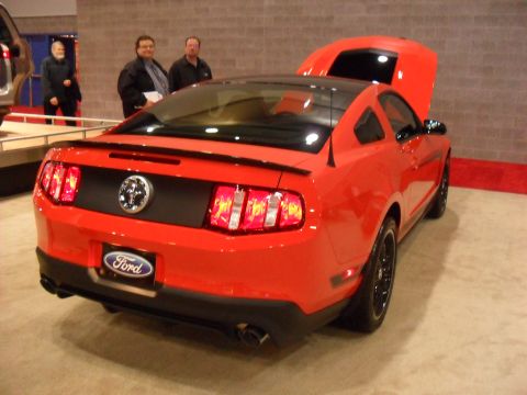 2012 Ford Mustang - Rear view of a red Ford Mustang with its hood open, showing a black spoiler and black wheels.
