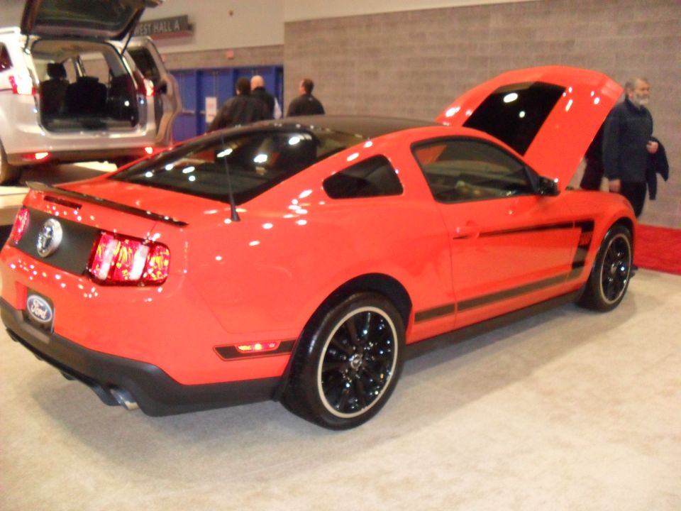Red Ford Mustang coupe rear three-quarter view with hood open at an auto show