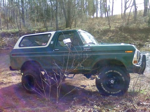 1979 Ford Bronco - 1978 Ford Bronco with a white top, parked off-road in a wooded area.