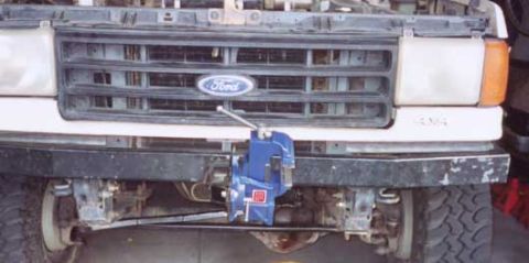 1987 Ford Bronco - A blue vise is clamped to the front bumper of a Ford truck.