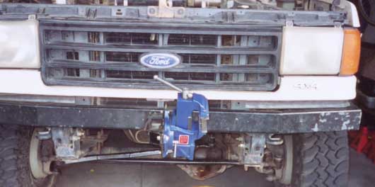 Blue bench vise bolted to the front bumper of a white Ford 4x4 below the grille