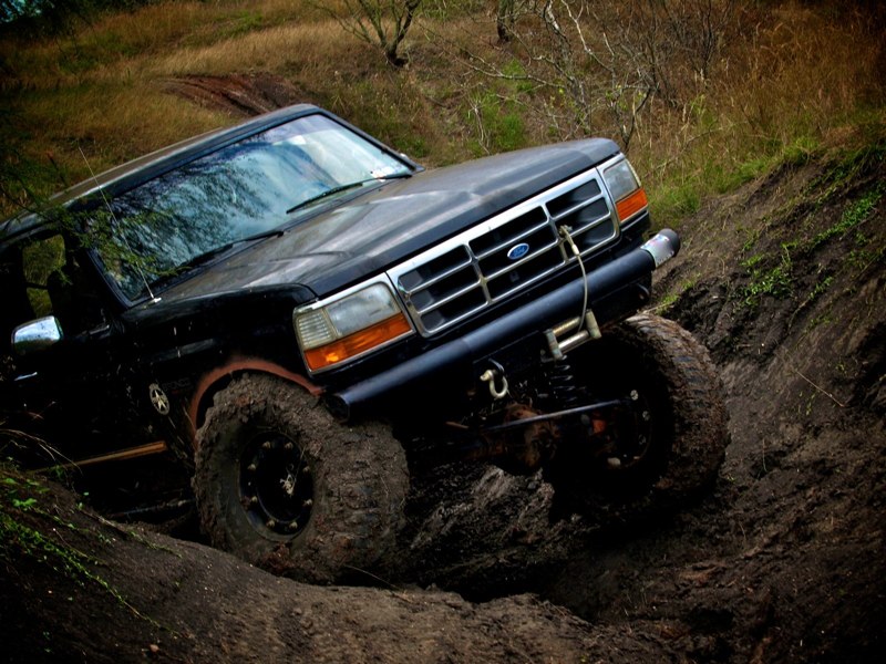 Black Ford Bronco with large mud tires navigating a muddy incline