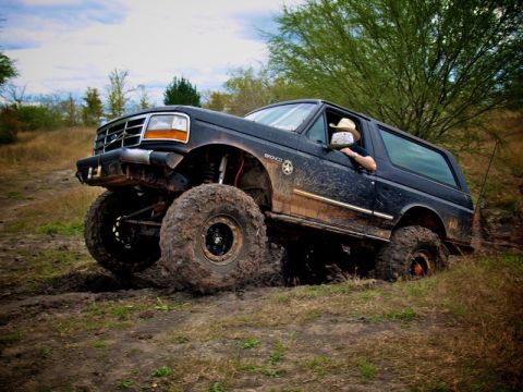1995 Ford Bronco - This lifted 1995 Ford Bronco is shown off-roading through a muddy terrain, demonstrating its capabilities.