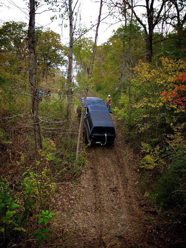 Dark 1995 Ford Bronco driving up a muddy hill in a wooded area