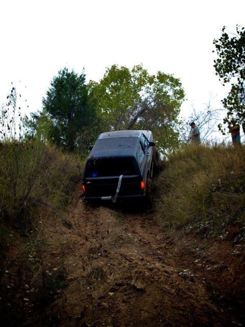 1995 Ford Bronco - A dark 1995 Ford Bronco navigates a challenging muddy hill, its off-road capabilities.