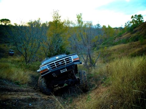 1995 Ford Bronco - A modified black Ford Bronco navigates a challenging off-road terrain with another vehicle in the background.