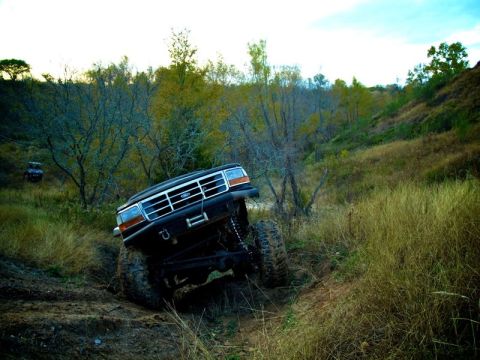 1995 Ford Bronco - A black 1995 Ford Bronco navigates a challenging off-road trail with another vehicle visible in the background.