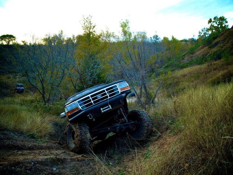 1995 Ford Bronco climbing a muddy hill off-road. Another vehicle is visible in the background