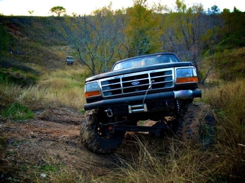 1995 Ford Bronco - This modified Ford Bronco is navigating a muddy, off-road trail with another vehicle in the distance.