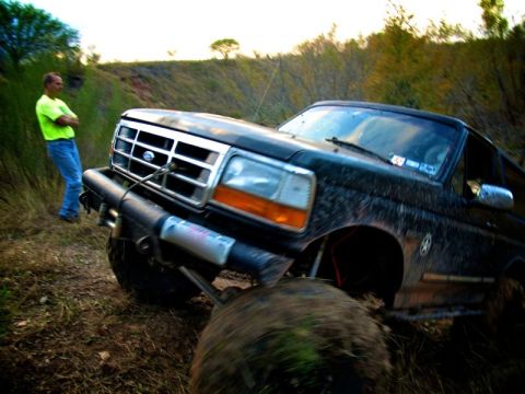 1995 Ford Bronco - A black Ford Bronco is stuck in the mud, with a winch cable attached to its front bumper.