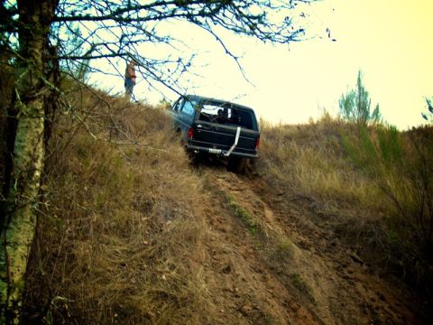 1995 Ford Bronco - Black 1995 Ford Bronco navigates a steep, muddy incline surrounded by dry grass and trees.
