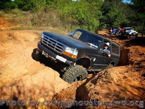 1995 Ford Bronco - A black Ford Bronco navigates a challenging off-road trail, with other vehicles and onlookers present.