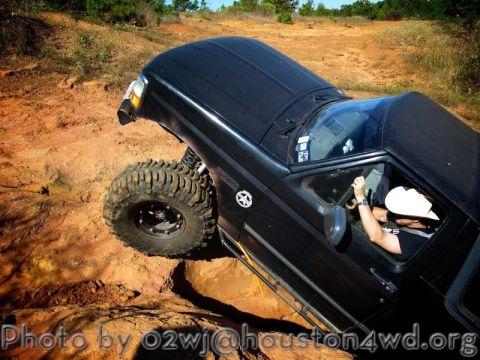 1995 Ford Bronco - A modified black SUV with oversized tires tackles a challenging off-road course.
