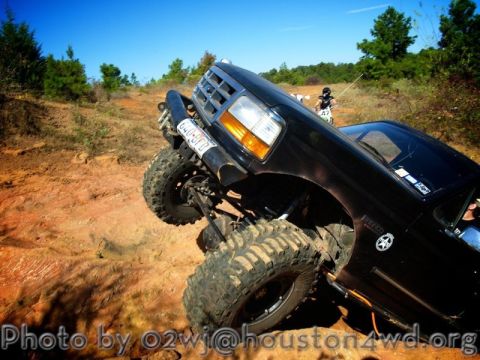 1995 Ford Bronco - A black Ford Bronco navigates a challenging off-road terrain with its tires digging into the dirt.