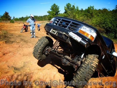 1995 Ford Bronco - A lifted black 1995 Ford Bronco navigates a challenging off-road course with two dirt bikes visible in the background.