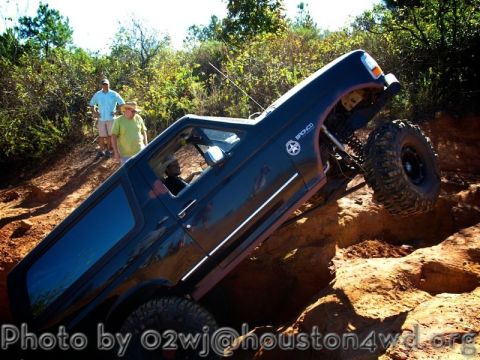 1995 Ford Bronco - A black 1995 Ford Bronco navigates a challenging off-road trail, with two onlookers observing from the side.