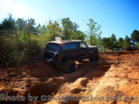 1995 Ford Bronco - A modified Ford Bronco navigates a challenging off-road trail under a clear blue sky.