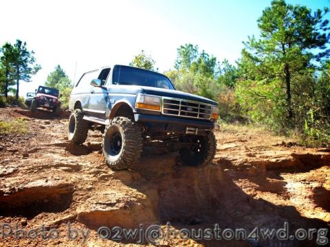 1995 Ford Bronco - A lifted Ford Bronco navigates an off-road trail, with a Jeep following in the background.