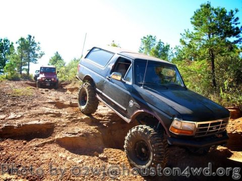 1995 Ford Bronco - A black 1995 Ford Bronco navigates a challenging off-road course, with a red Jeep in the background.
