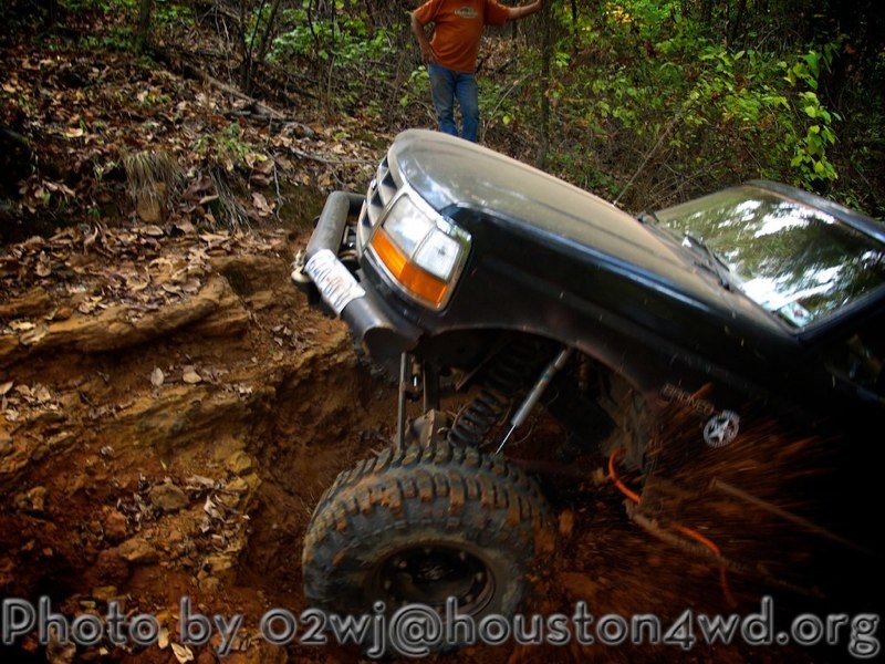 Black off-road SUV climbing a muddy hill, front wheel angled up