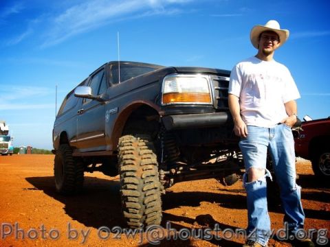 1995 Ford Bronco - A man poses with his lifted Ford Bronco on a dirt lot under a blue sky.