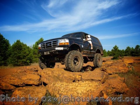 1995 Ford Bronco - A black Ford Bronco navigates a challenging rocky trail under a blue sky.