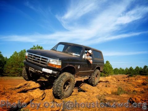 1995 Ford Bronco - A black 1995 Ford Bronco navigates a rocky trail under a bright blue sky.