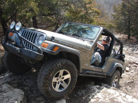 2005 Jeep Wrangler - A tan Jeep Wrangler Rubicon navigates a rocky trail with its driver visible.
