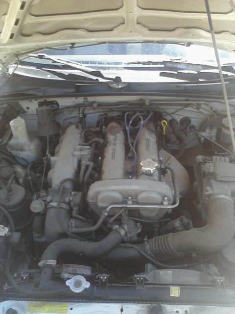 1968 Ford Mustang - Overhead engine bay view of a Mazda DOHC 16-valve four-cylinder, showing the cast valve cover, a Mazda-branded intake manifold, blue plug w…