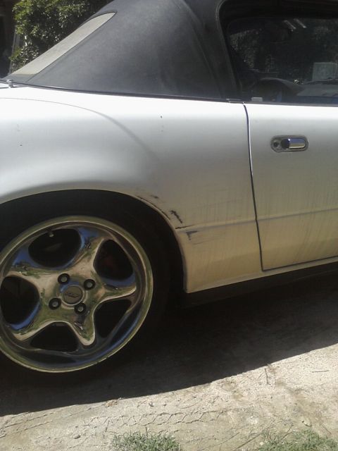 1968 Ford Mustang - Close-up of the front fender, door and chrome five-spoke wheel on a white convertible with the black soft top up, showing scraped paint and…