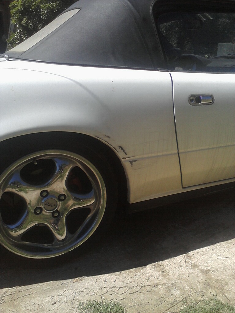 Scraped fender and door of white convertible with chrome five-spoke wheel